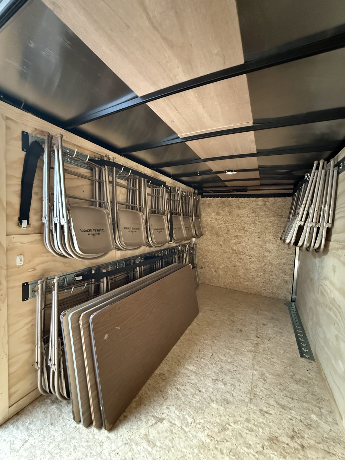 Inside the trailer: folding chairs hanging on custom wall racks with banquet tables stored alongside